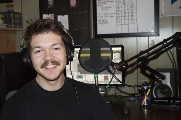 Male audio engineer wearing headphones, smiling in a recording studio with a microphone and computer setup.